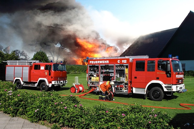 Zwei Feueerwehrfahrzeuge stehen vor einem brennenden Reetdachhaus, aus dem die Flammen schlagen.s