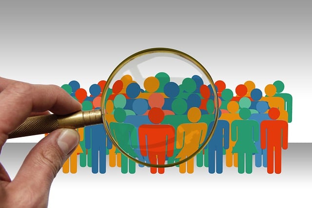 eine Hand hält eine Lupe. Zu sehen sind stilisierte bunte Personen, z.T. vergrößert.